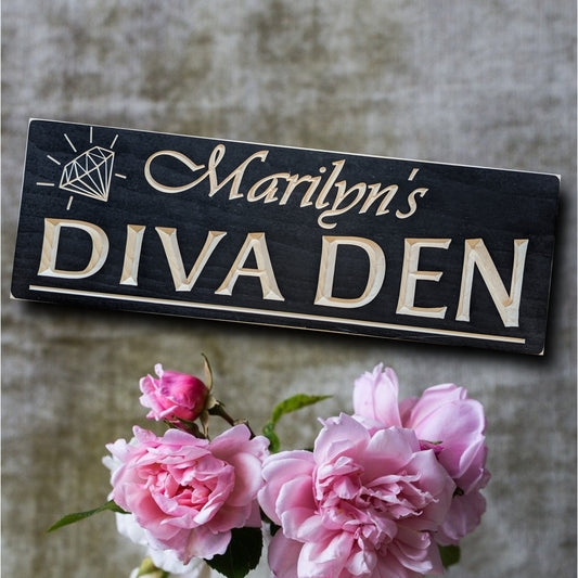 A Black painted sign with carved letters featuring a diamond in the left corner with a personalized name on top and the inscription "Diva Den" on the bottom line