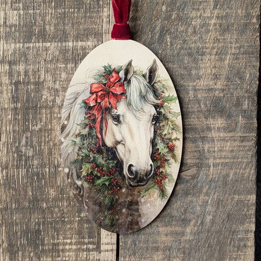 Decorative ornament with a horse's head wearing a red bow and floral wreath on a wooden background.
