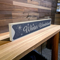 A wood sign in white and grey with the inscription Winter Wonderland and snowflakes